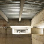 Isolatori sismici neri tra plinti in calcestruzzo, travi e lamiera grecata viste dal vano fondazioni di un edificio